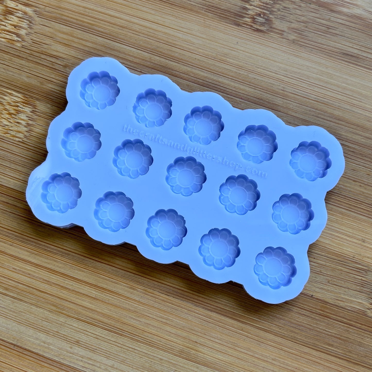 Blue silicone mold with flower-shaped cavities on a wooden surface
