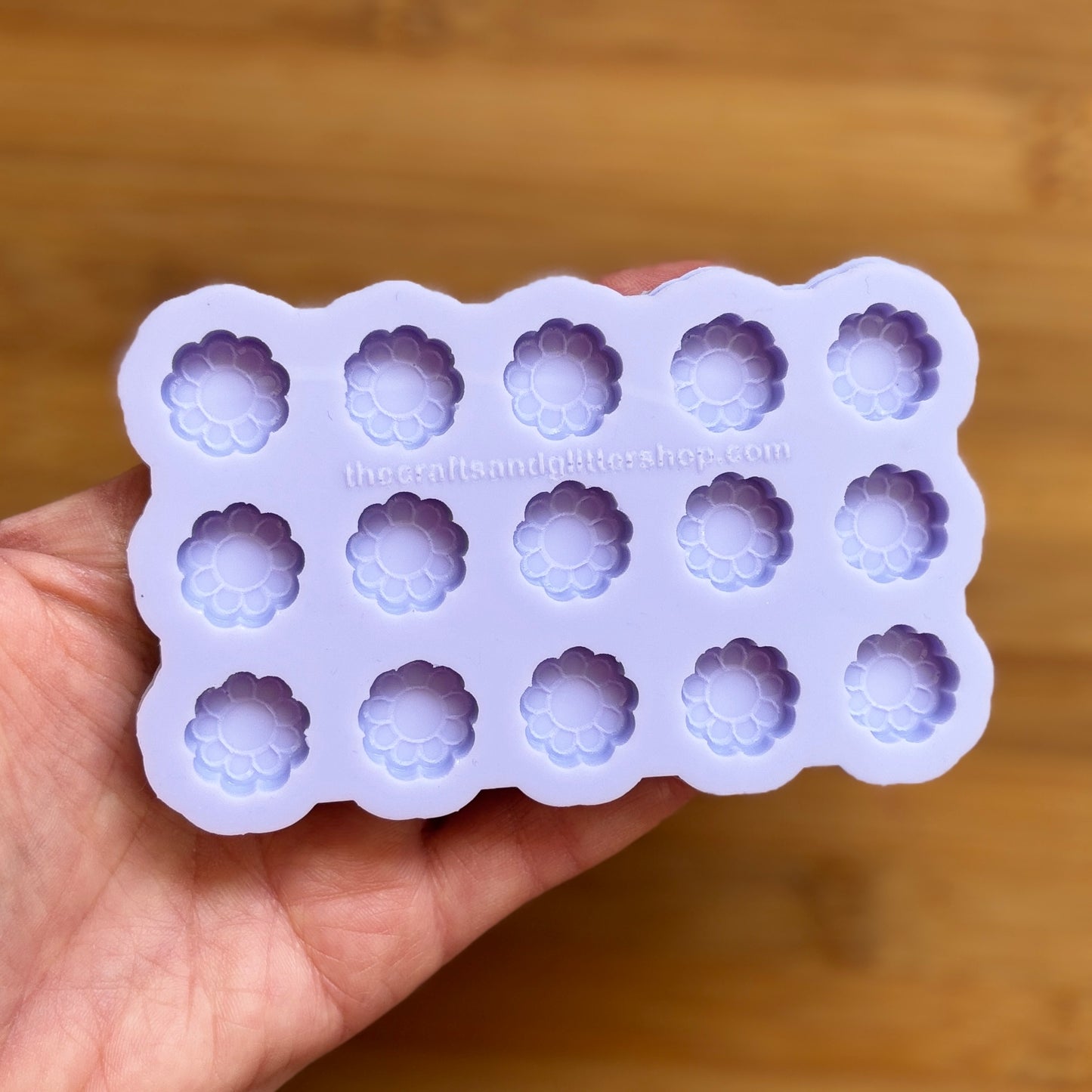 Silicone mold with flower-shaped cavities held in a hand against a wooden background