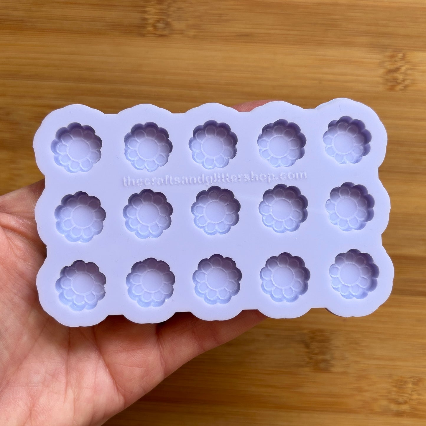 Silicone mold with flower-shaped cavities held by a hand on a wooden surface