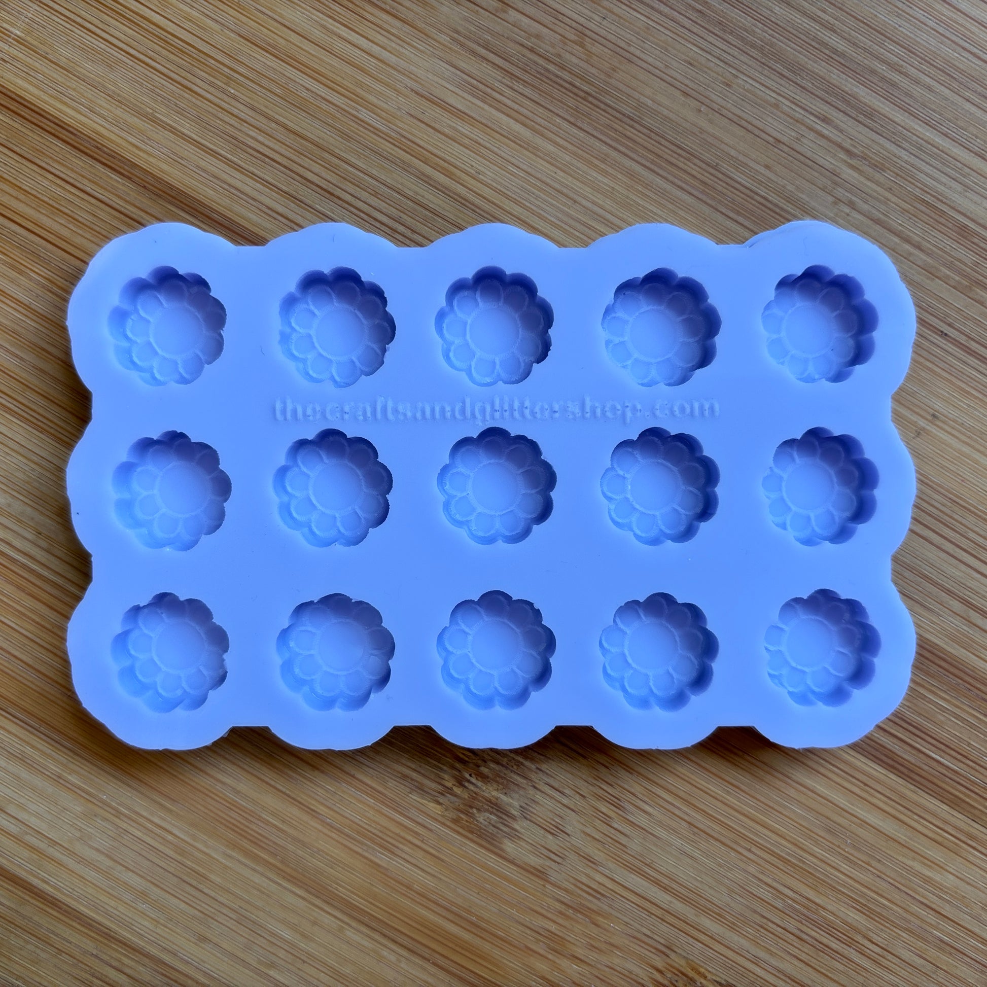 Blue silicone mold with flower-shaped cavities on a wooden surface