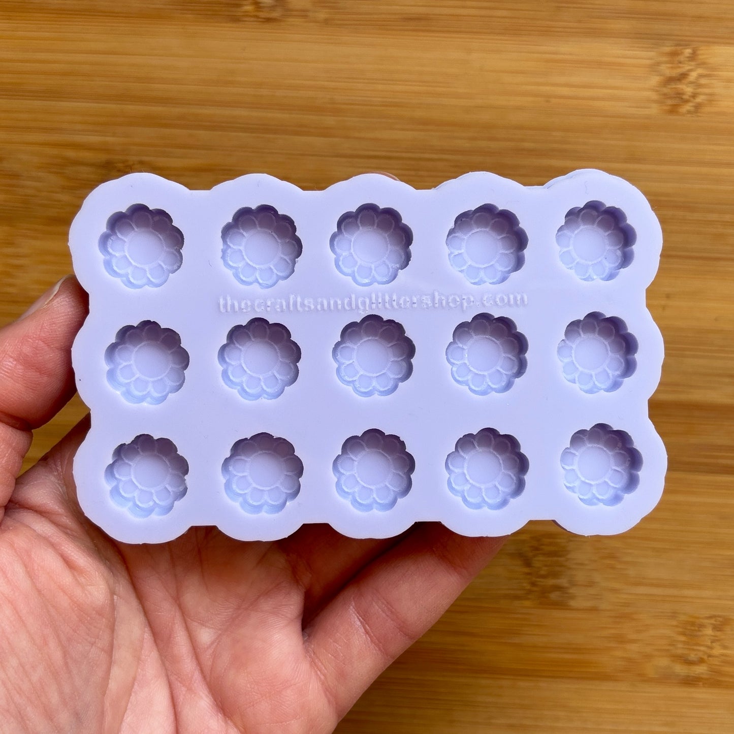 Silicone mold with flower-shaped cavities held by a hand on a wooden surface
