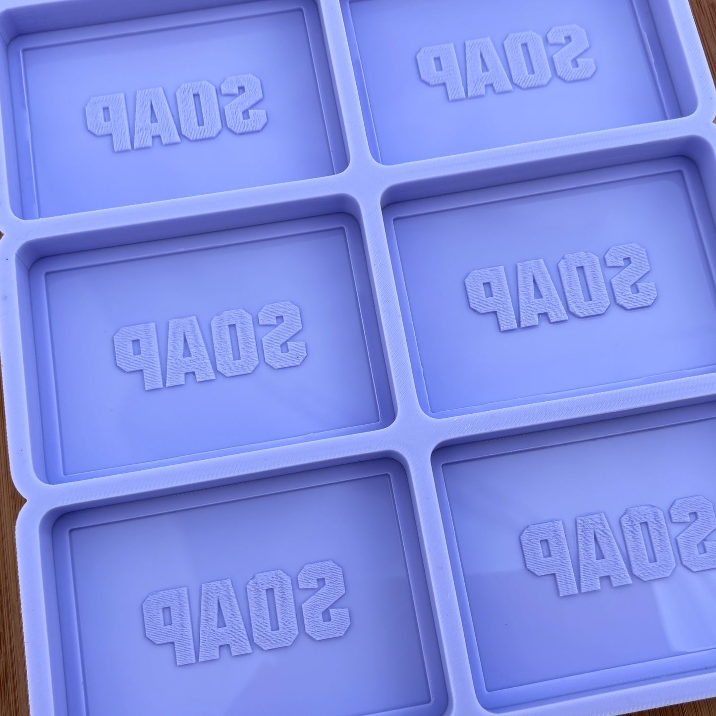 Purple soap mold with 'SOAP' text in each cavity on a wooden surface.