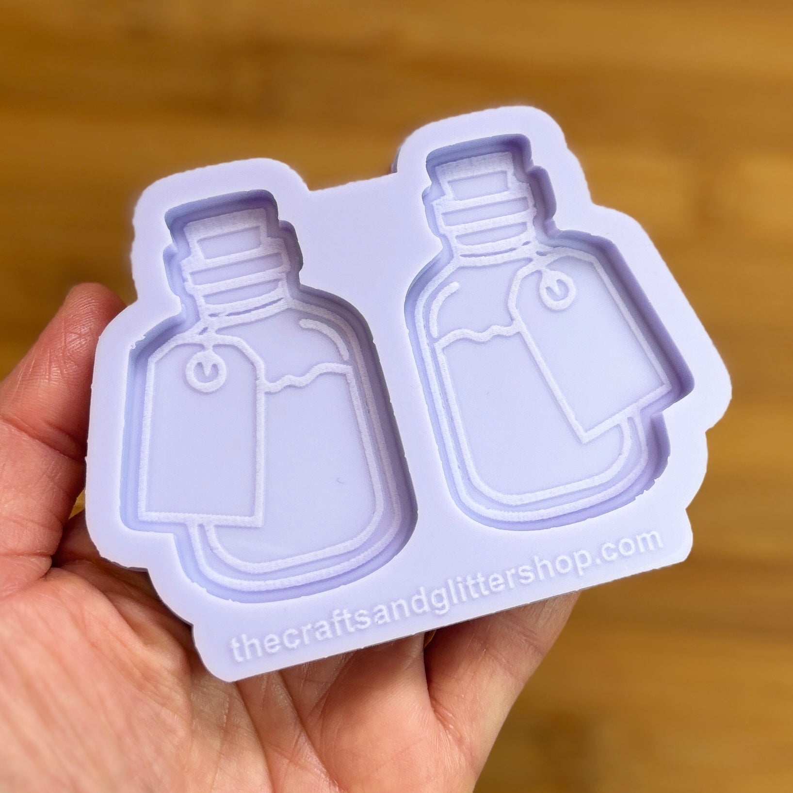Hand holding a silicone mold shaped like two bottles with 'thecraftsandglittershop.com' branding.