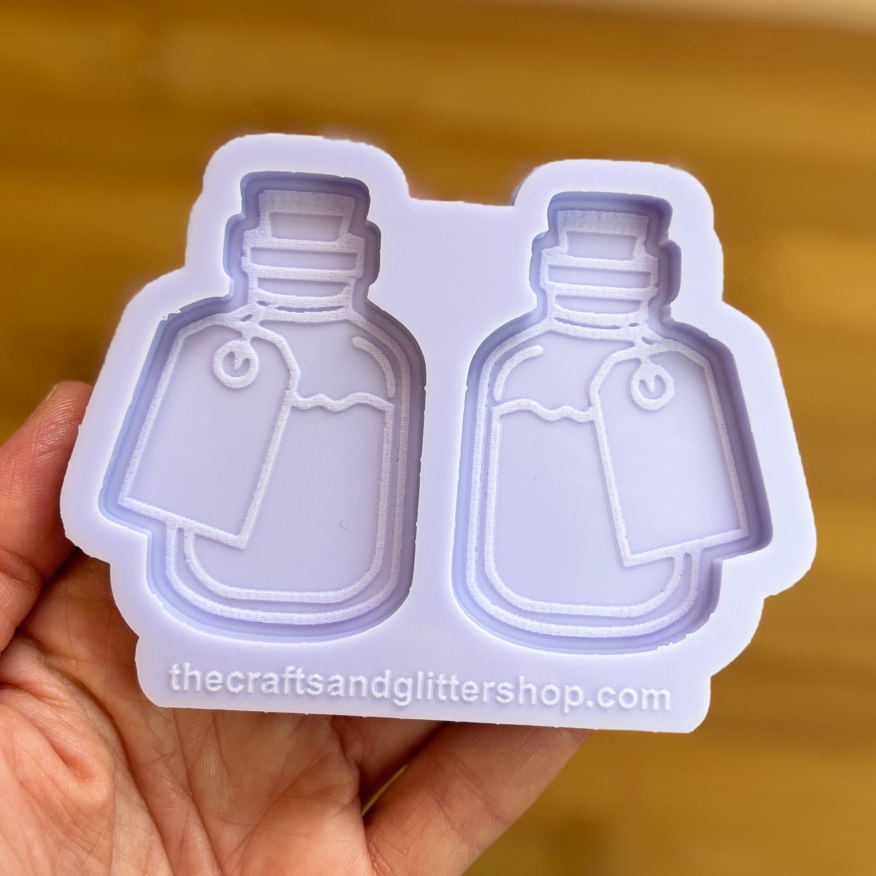Two bottle-shaped silicone molds held by a hand with a blurred background.