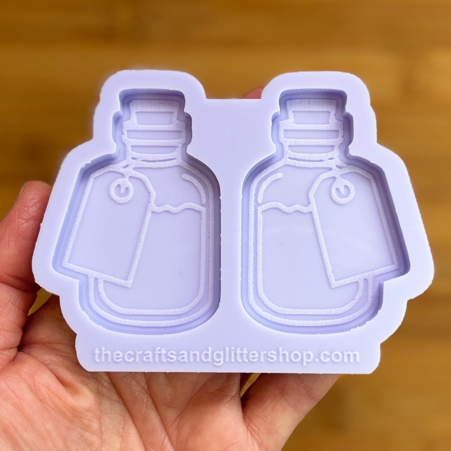 Two bottle-shaped silicone molds held by a hand with a blurred background.