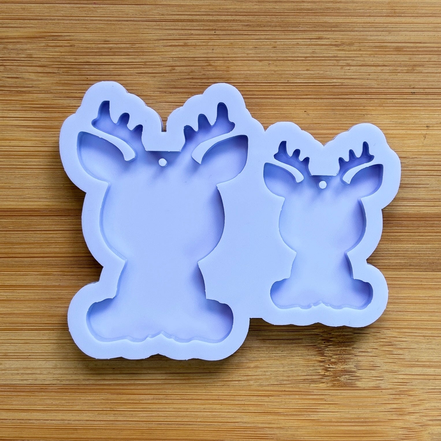 Reindeer silhouette Silicone Mold with 2 cavities of different sizes. The cavity has a hole in it. The mols is made with Food Safe Silicone suitable for both food and craft projects.