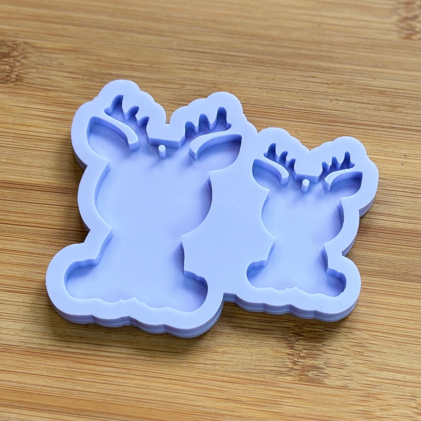 Reindeer silhouette Silicone Mold with 2 cavities of different sizes. The cavity has a hole in it. The mols is made with Food Safe Silicone suitable for both food and craft projects.