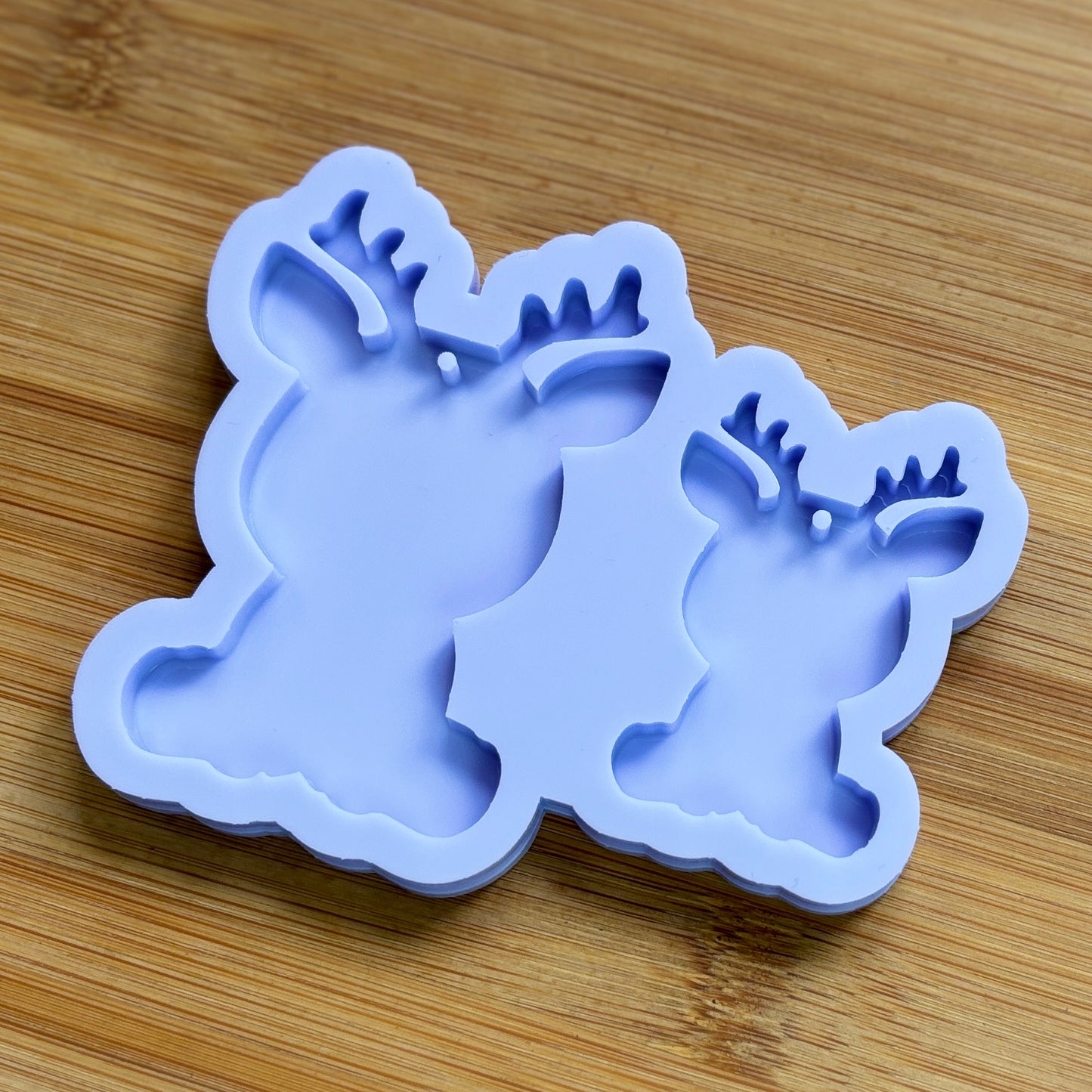 Reindeer silhouette Silicone Mold with 2 cavities of different sizes. The cavity has a hole in it. The mols is made with Food Safe Silicone suitable for both food and craft projects.