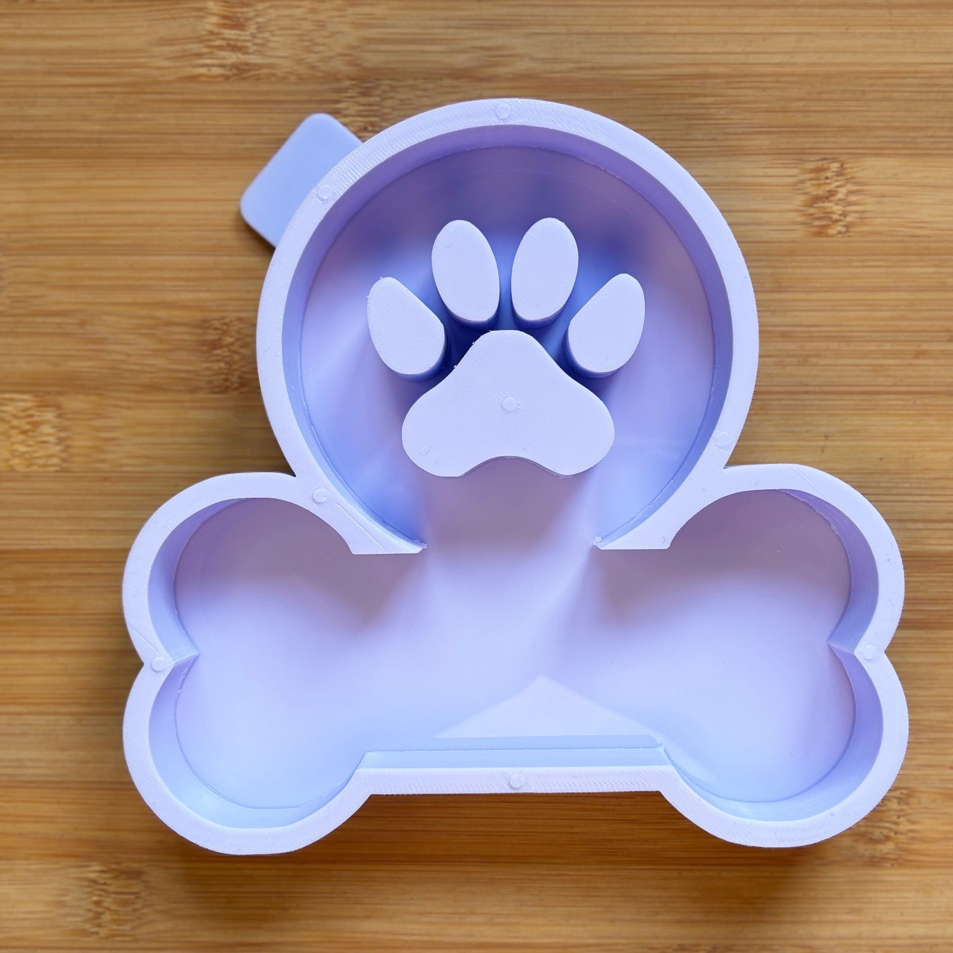 Silicone mold shaped like a bone with a paw print on a wooden surface