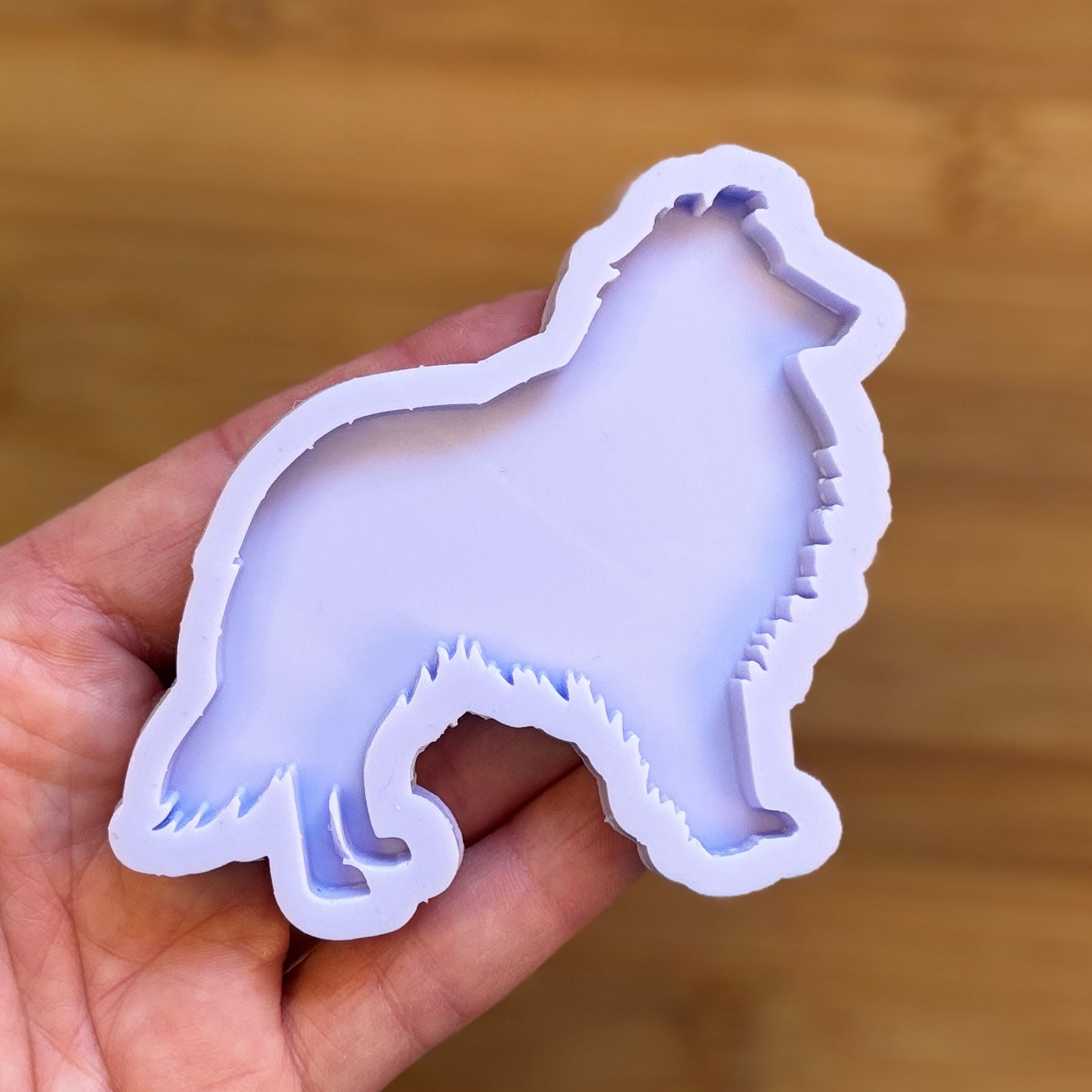 Hand holding a dog-shaped silicone mold against a wooden background