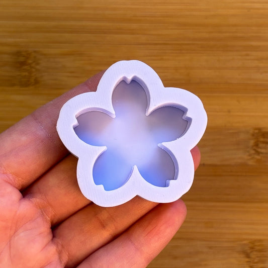 Flower-shaped silicone mold held in a hand against a wooden background
