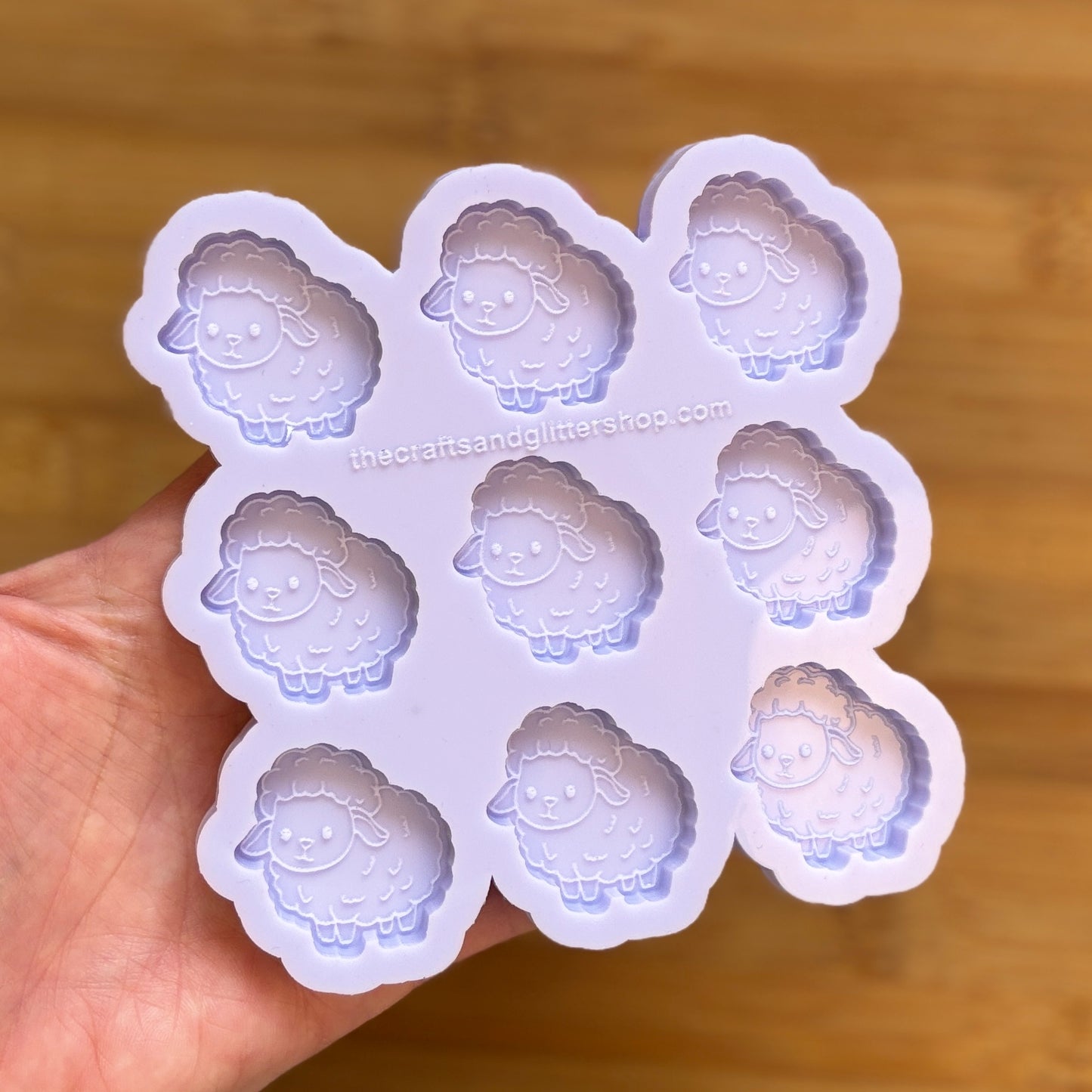 Sheep-shaped silicone mold held by a hand on a wooden surface