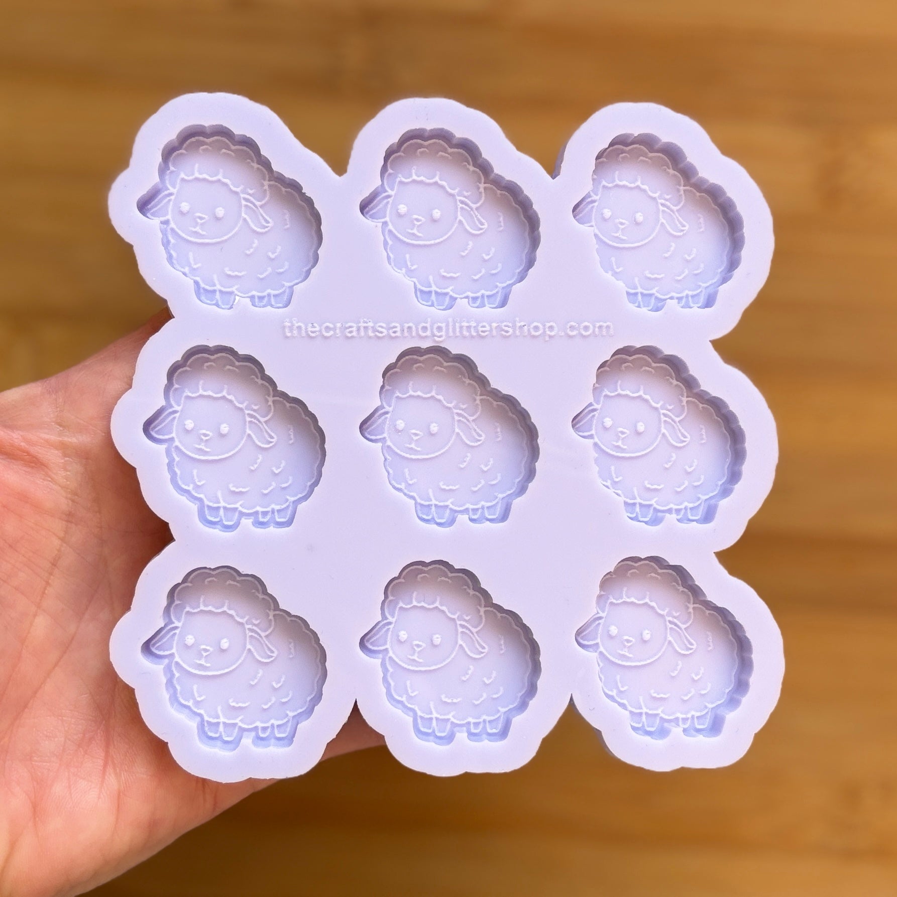 Silicone mold with sheep designs held by a hand on a wooden surface