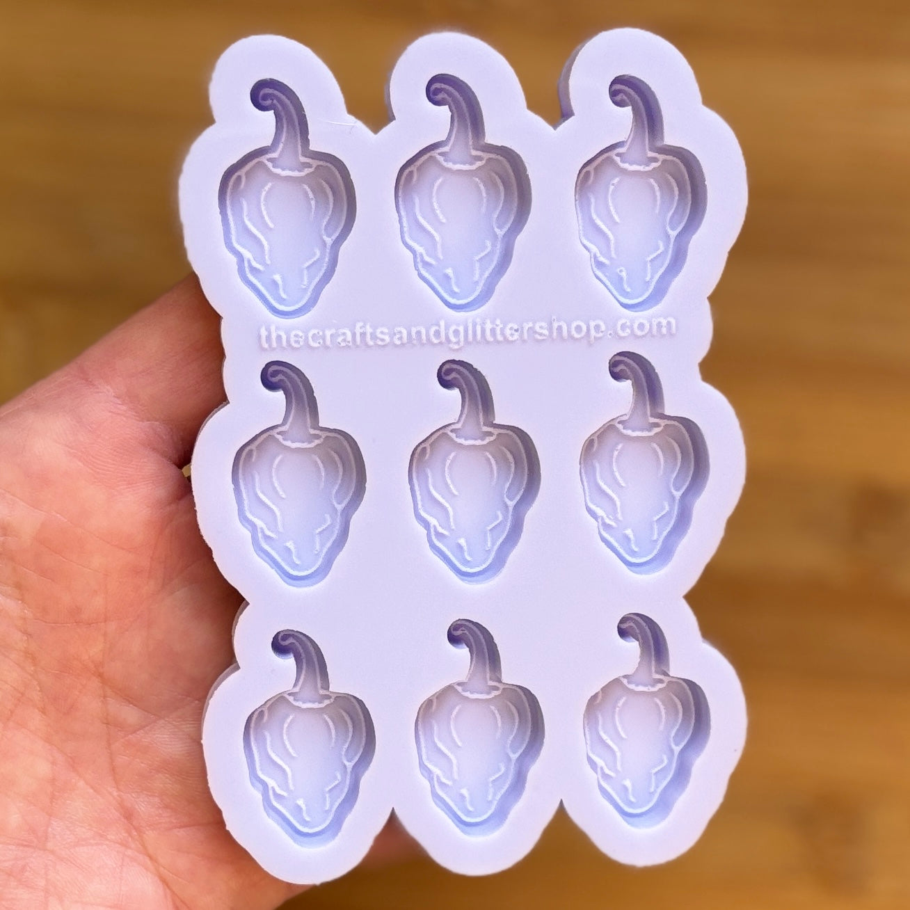 Hand holding a silicone mold with habanero shapes on a wooden surface