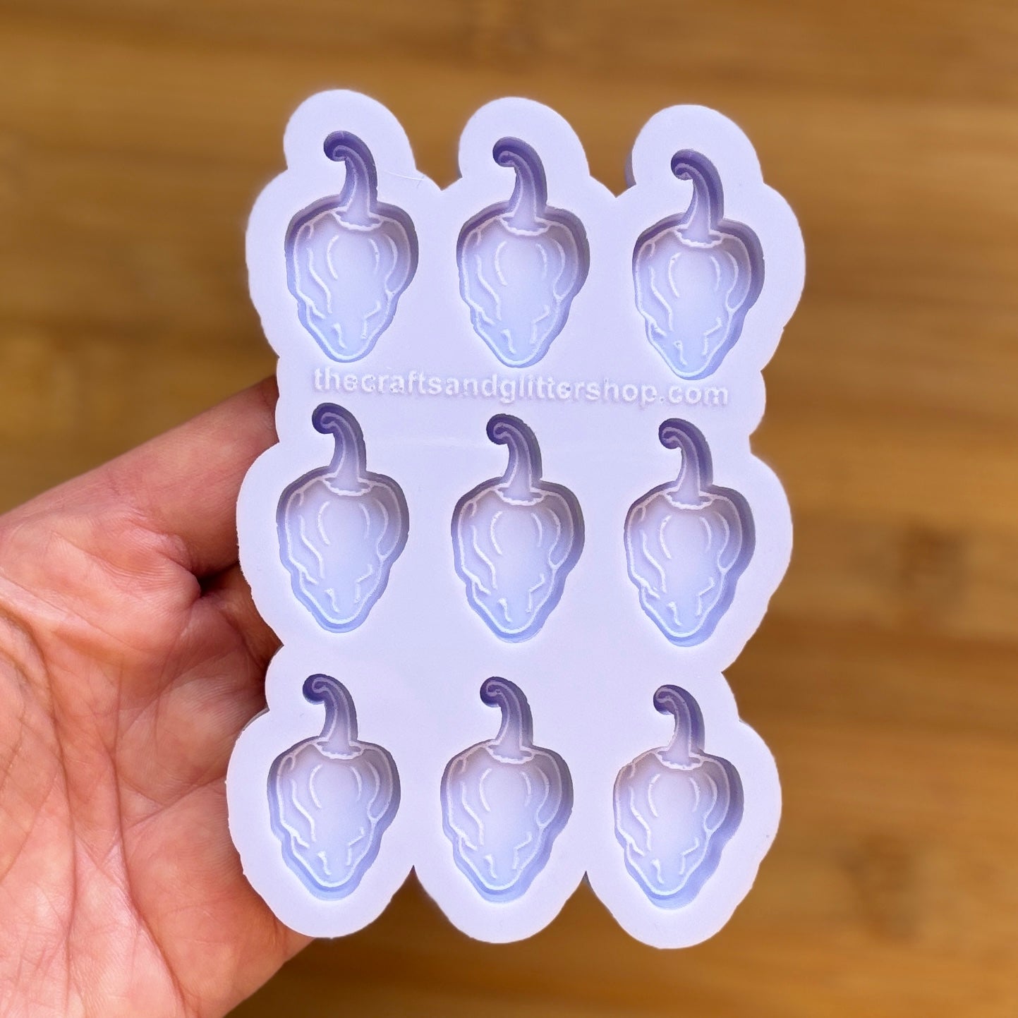 Hand holding a silicone mold with habanero-shaped cavities against a wooden background