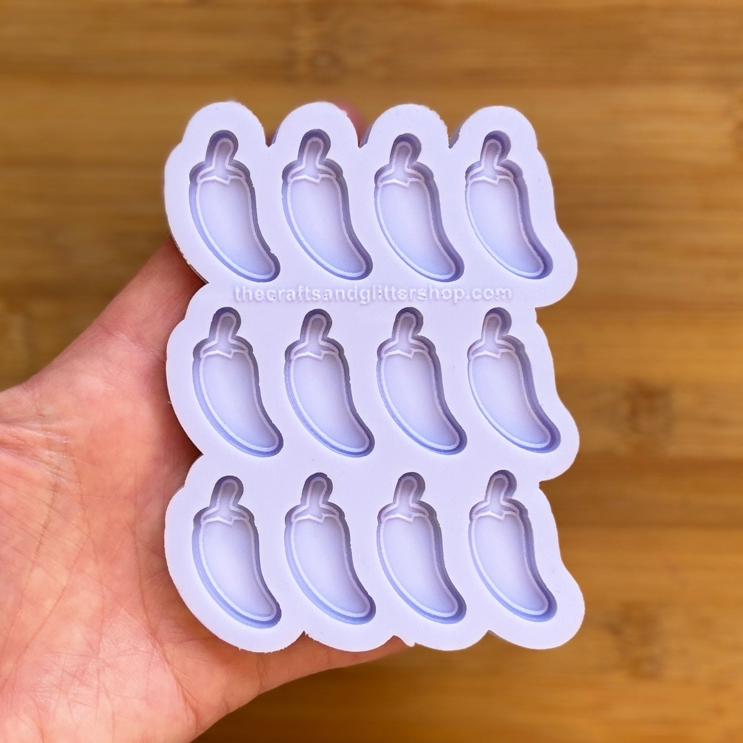 Hand holding a silicone mold with jalapeno pepper shapes against a wooden background