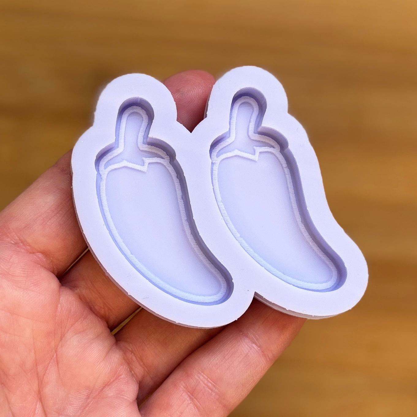 silicone chili pepper molds held in a hand against a wooden background