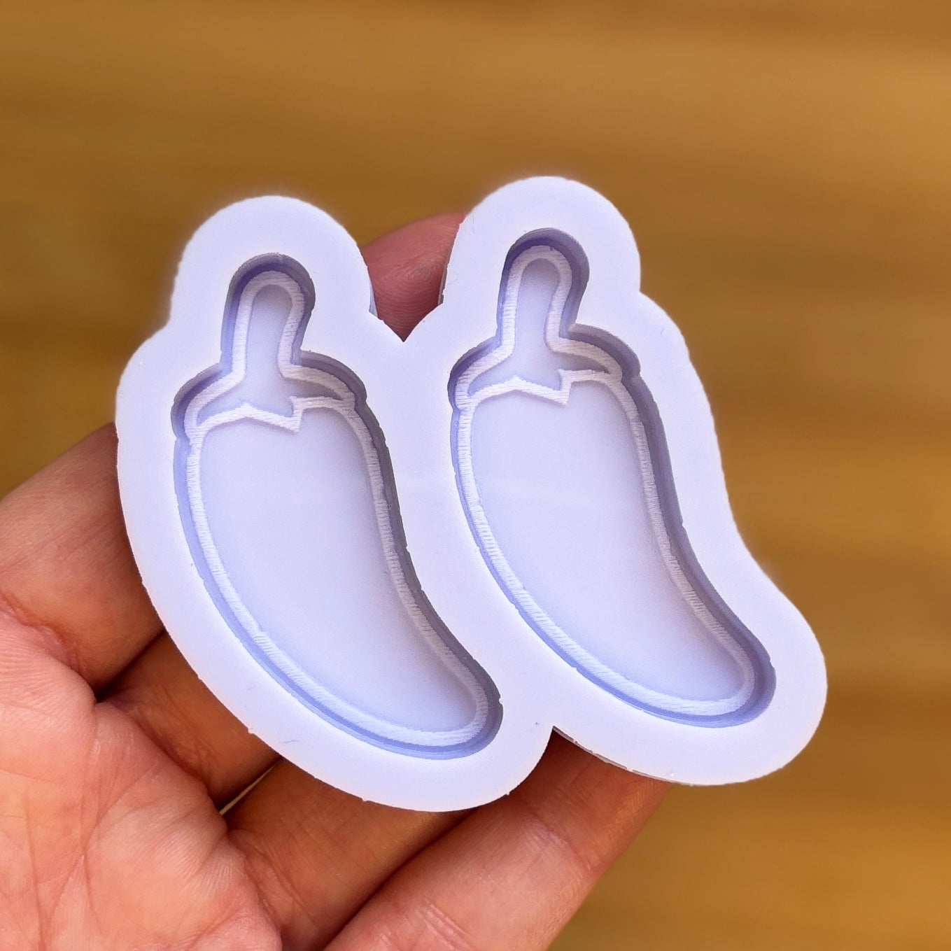 chili pepper-shaped silicone mold held in a hand against a brown background