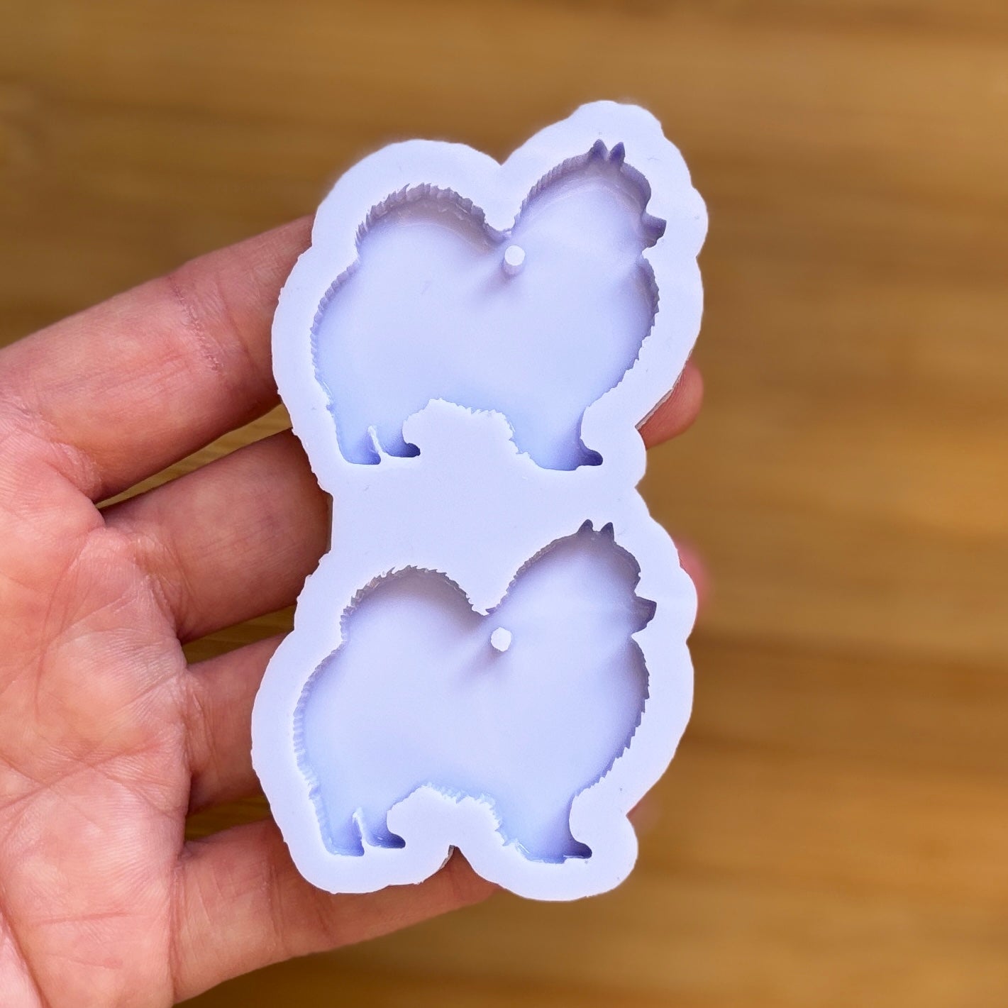 Hand holding a silicone mold with dog shapes on a wooden surface