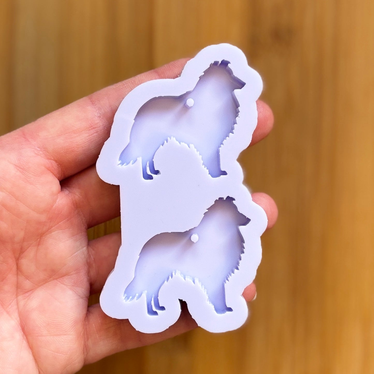 Hand holding a shetland sheepdog shaped silicone mold against a wooden background