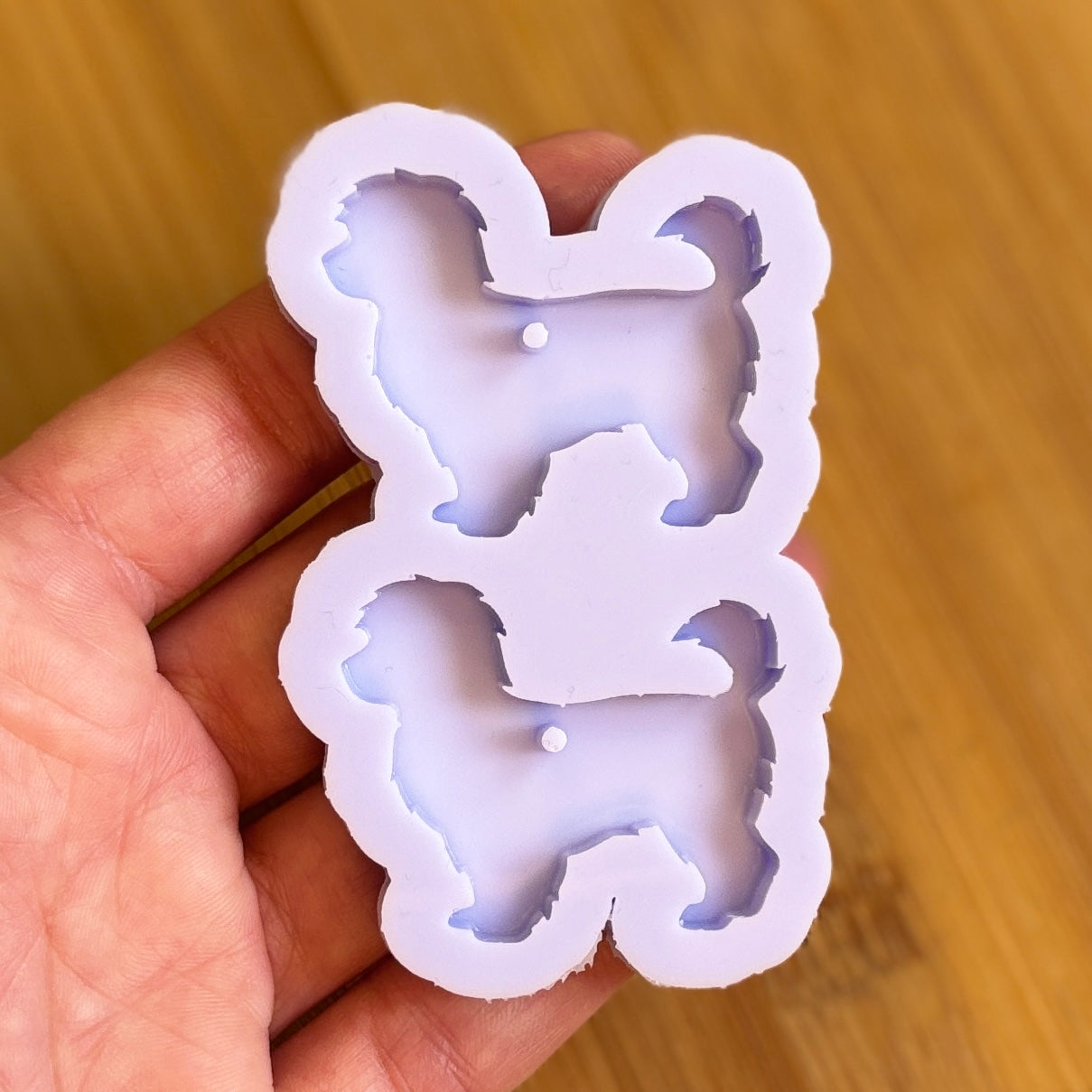 Hand holding a silicone mold with dog shapes on a wooden surface