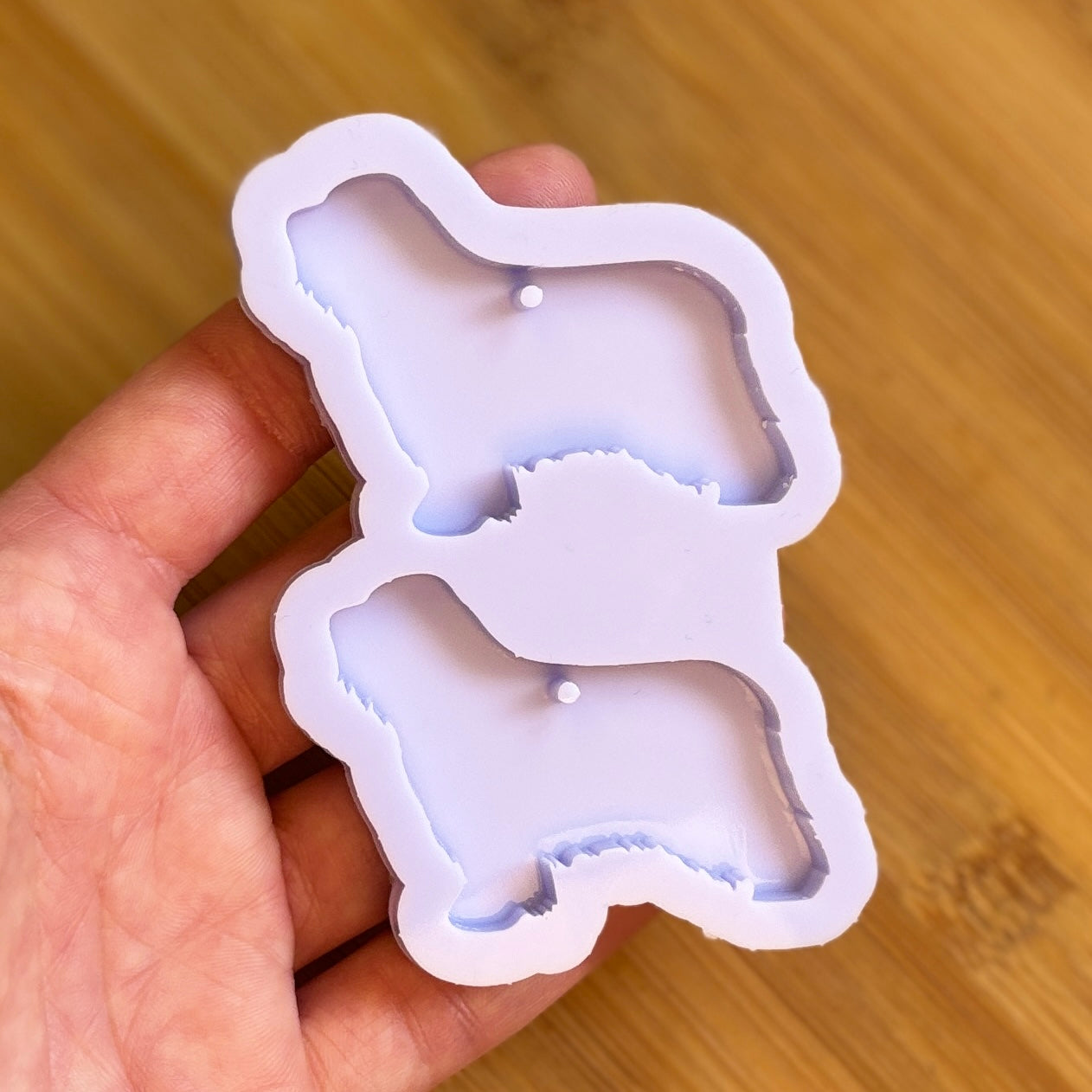 Hand holding a silicone mold shaped like a dog on a wooden surface