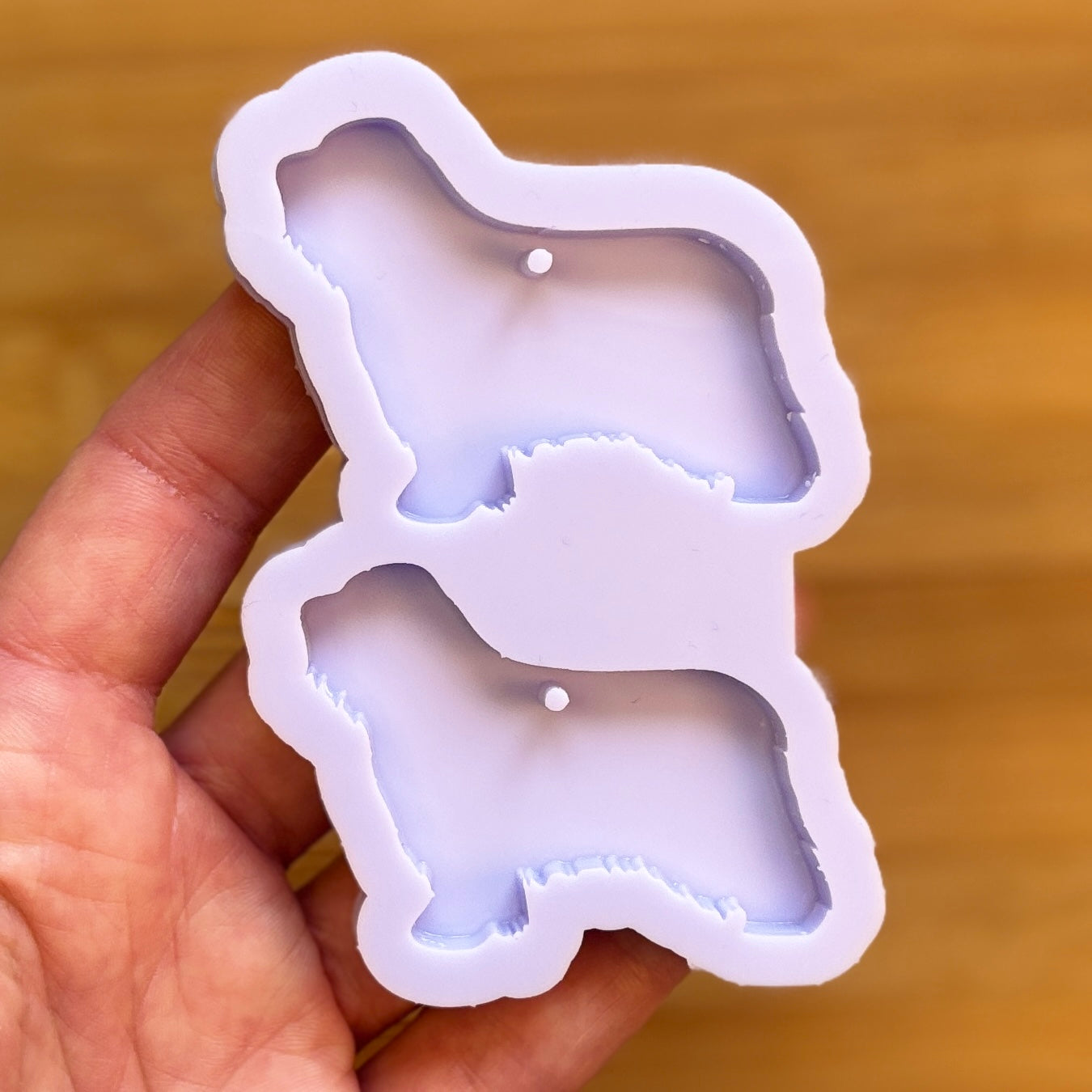 Hand holding a silicone mold shaped like a dog on a wooden surface