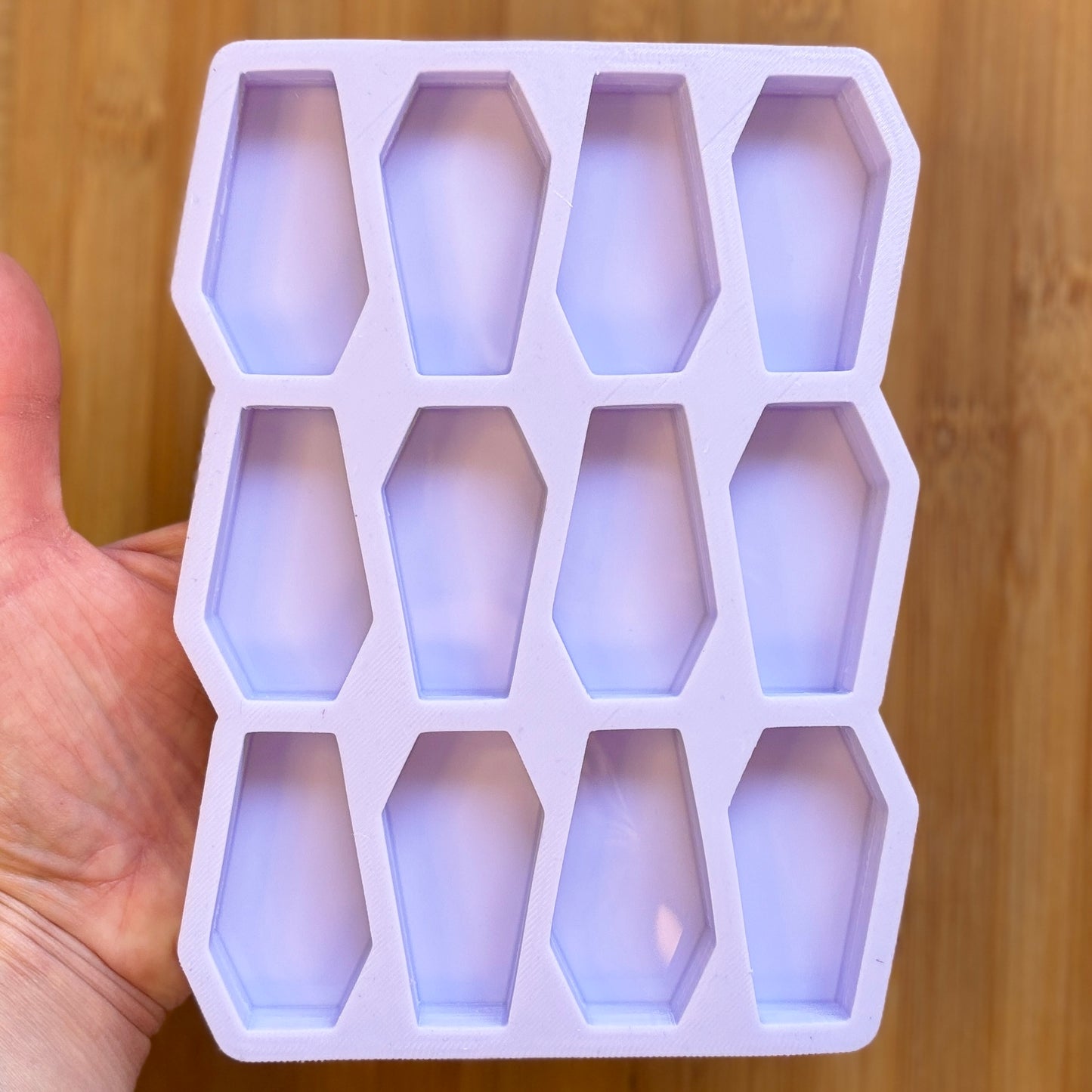 Silicone mold with coffin shapes held by a hand on a wooden background