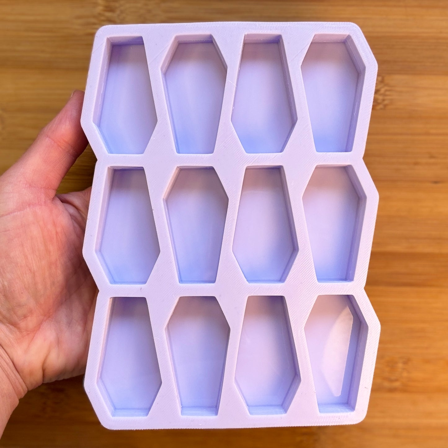Silicone ice cube tray with coffin shapes held by a hand on a wooden surface