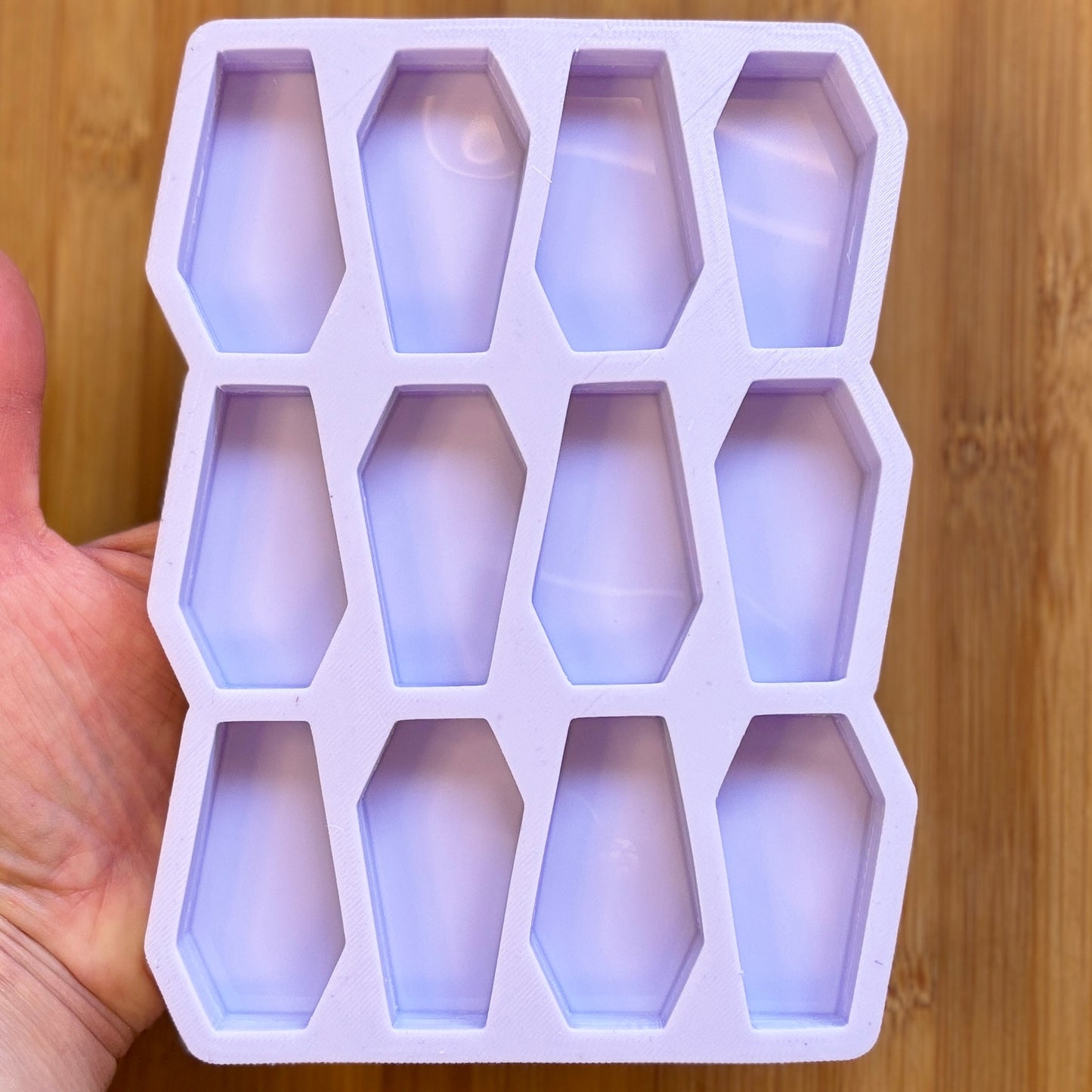 Silicone mold with coffin-shaped cavities held by a hand on a wooden surface