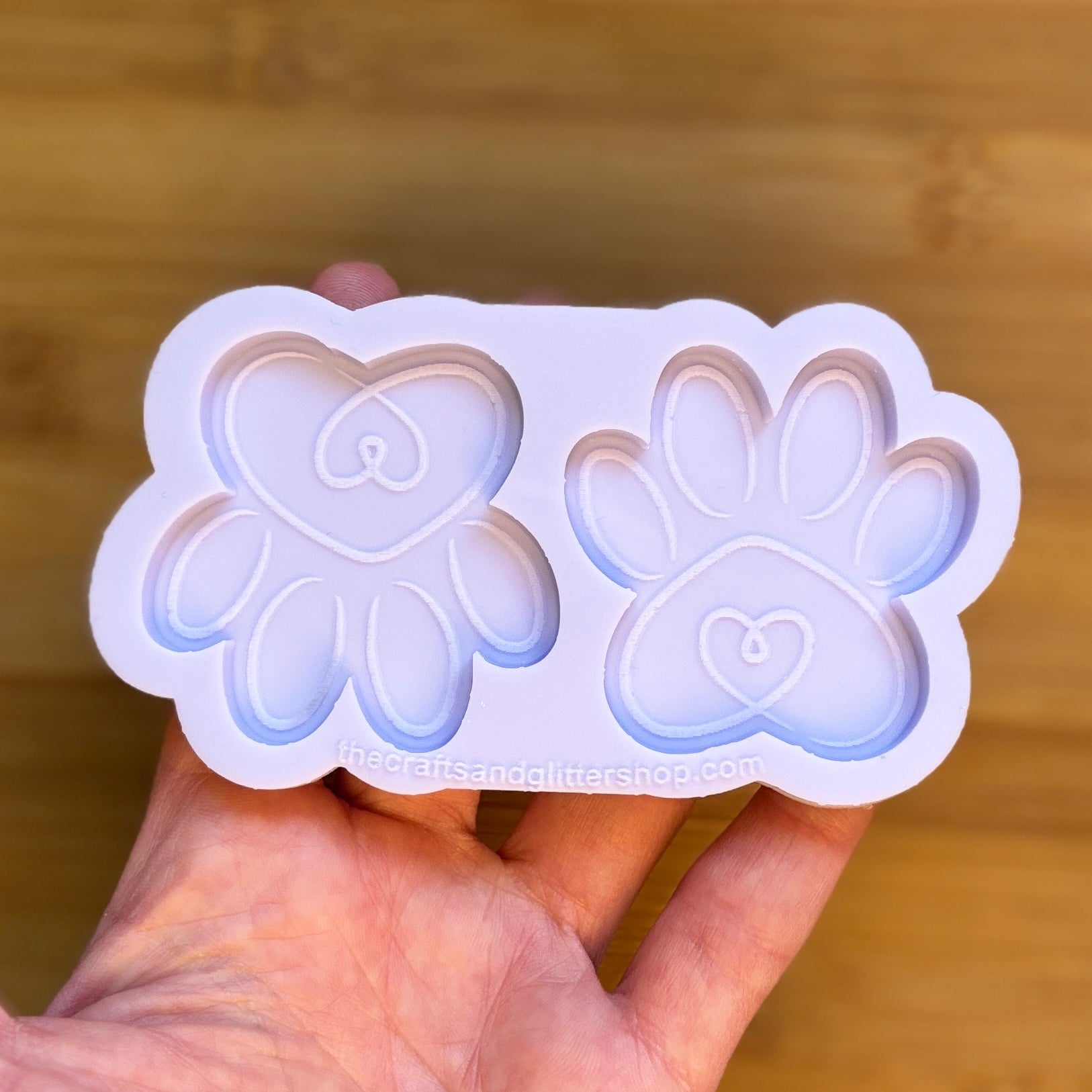 Hand holding a silicone mold with paw and heart designs against a wooden background