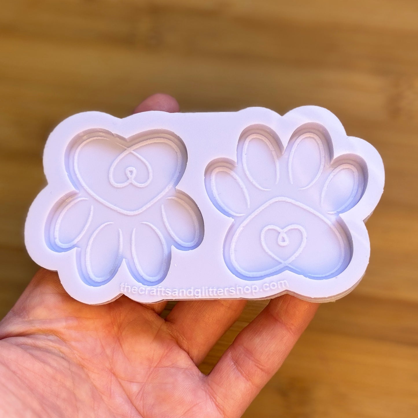 Silicone mold with heart and paw designs held in a hand against a wooden background