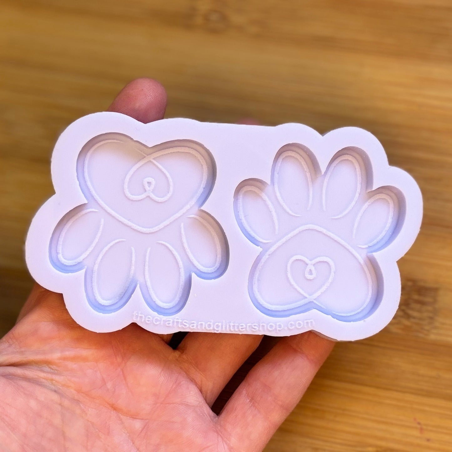 Silicone mold with heart and paw print shapes held in a hand on a wooden surface