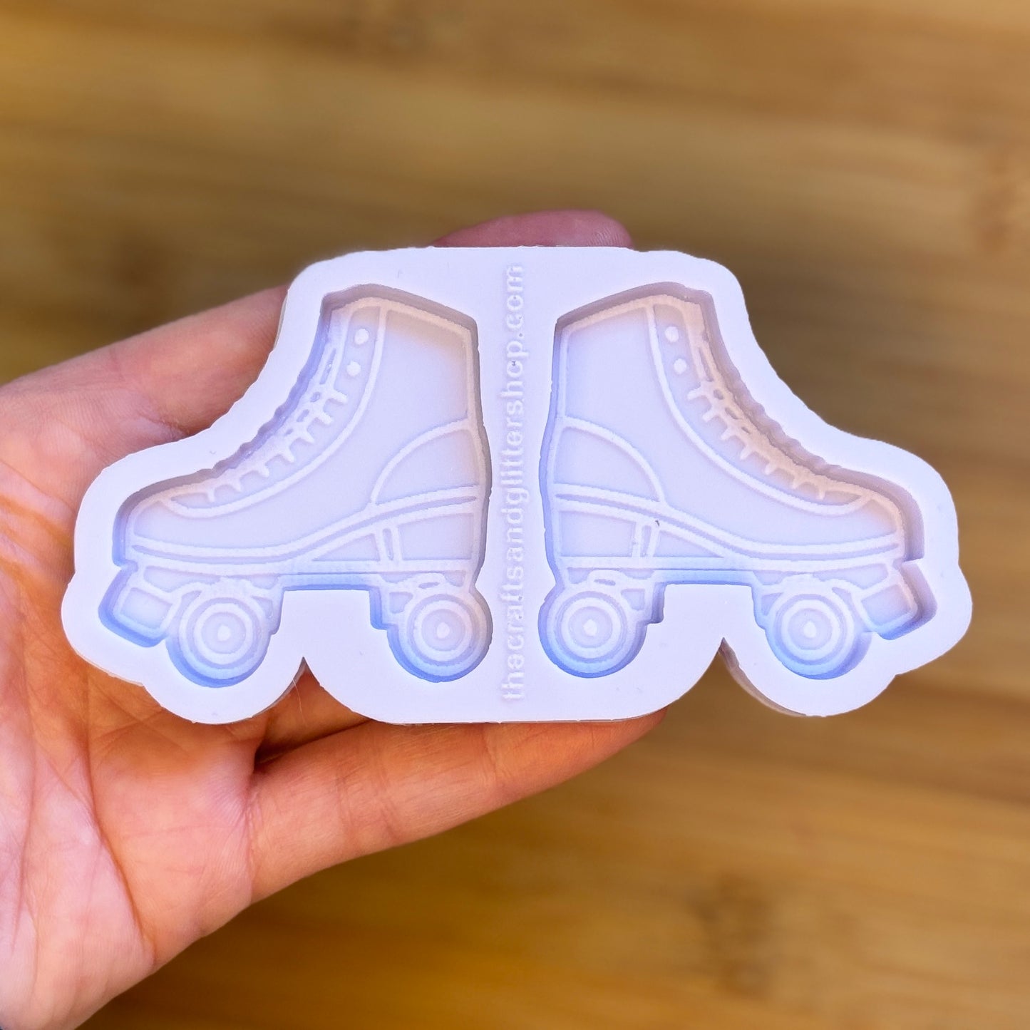 Hand holding a silicone mold shaped like roller skates on a wooden surface