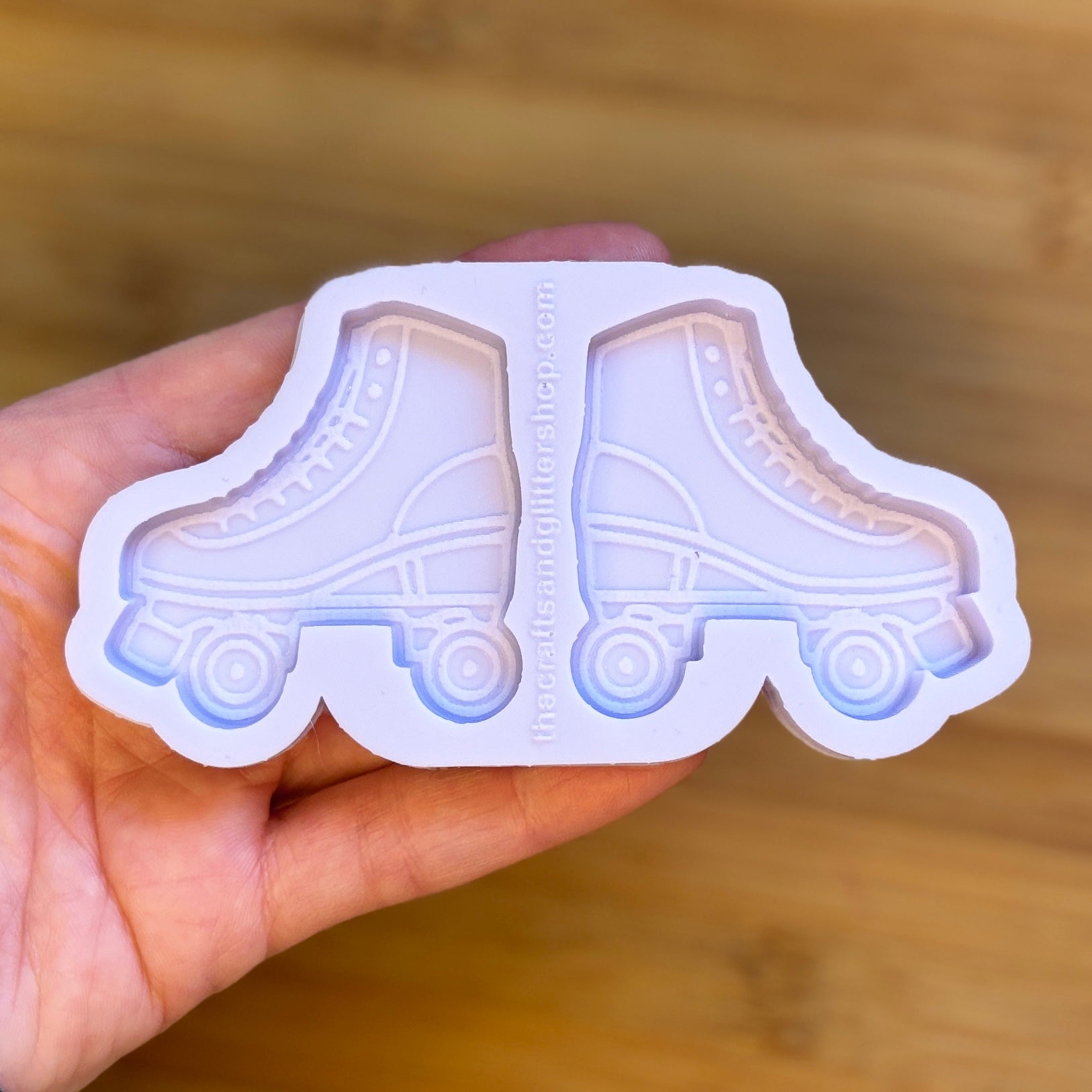 Hand holding a silicone mold shaped like roller skates on a wooden surface