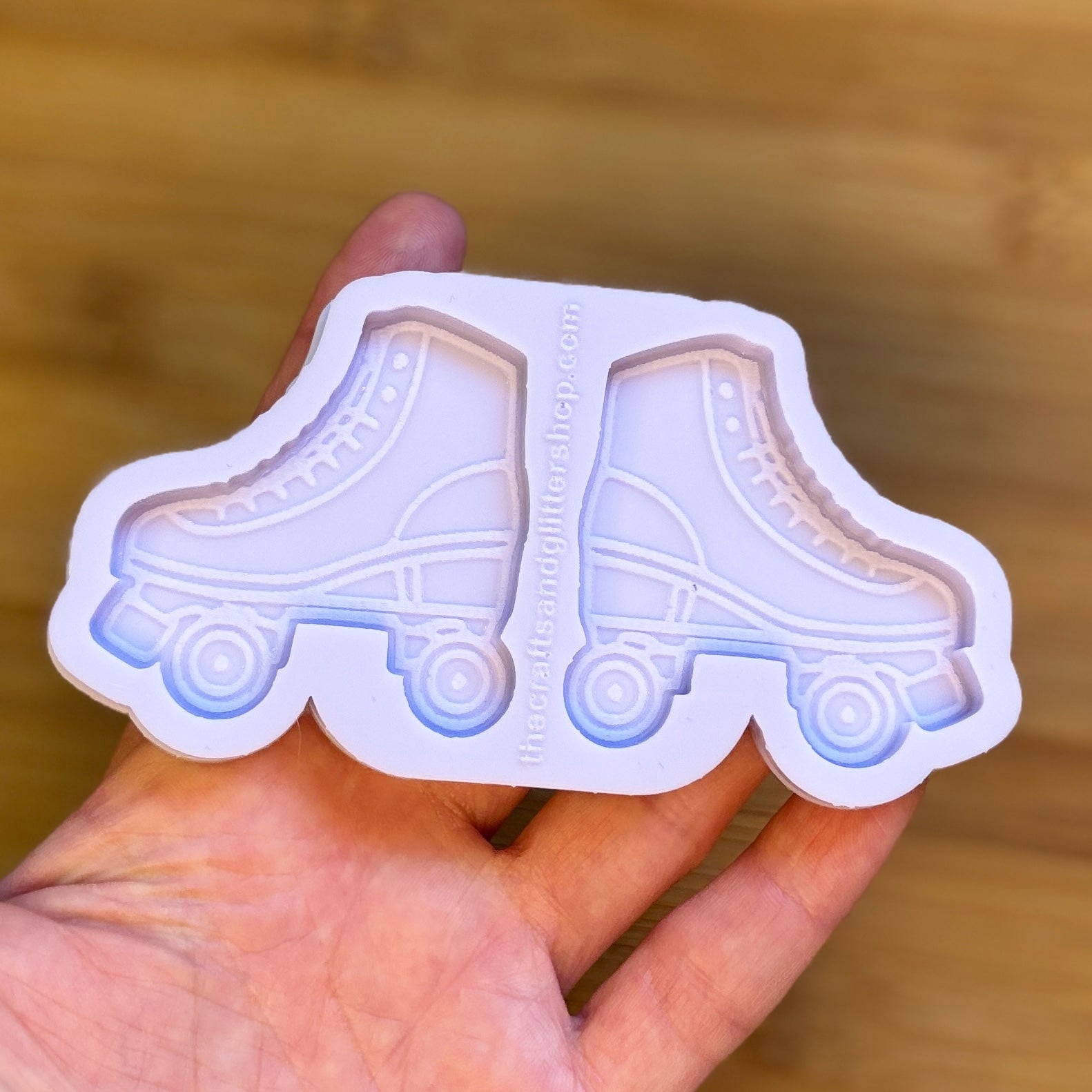 Hand holding a silicone mold shaped like roller skates on a wooden surface