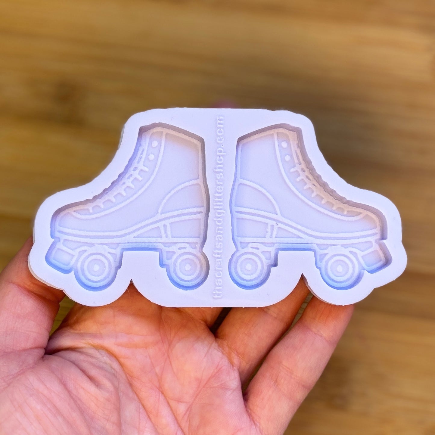 Hand holding a silicone mold shaped like roller skates on a wooden surface