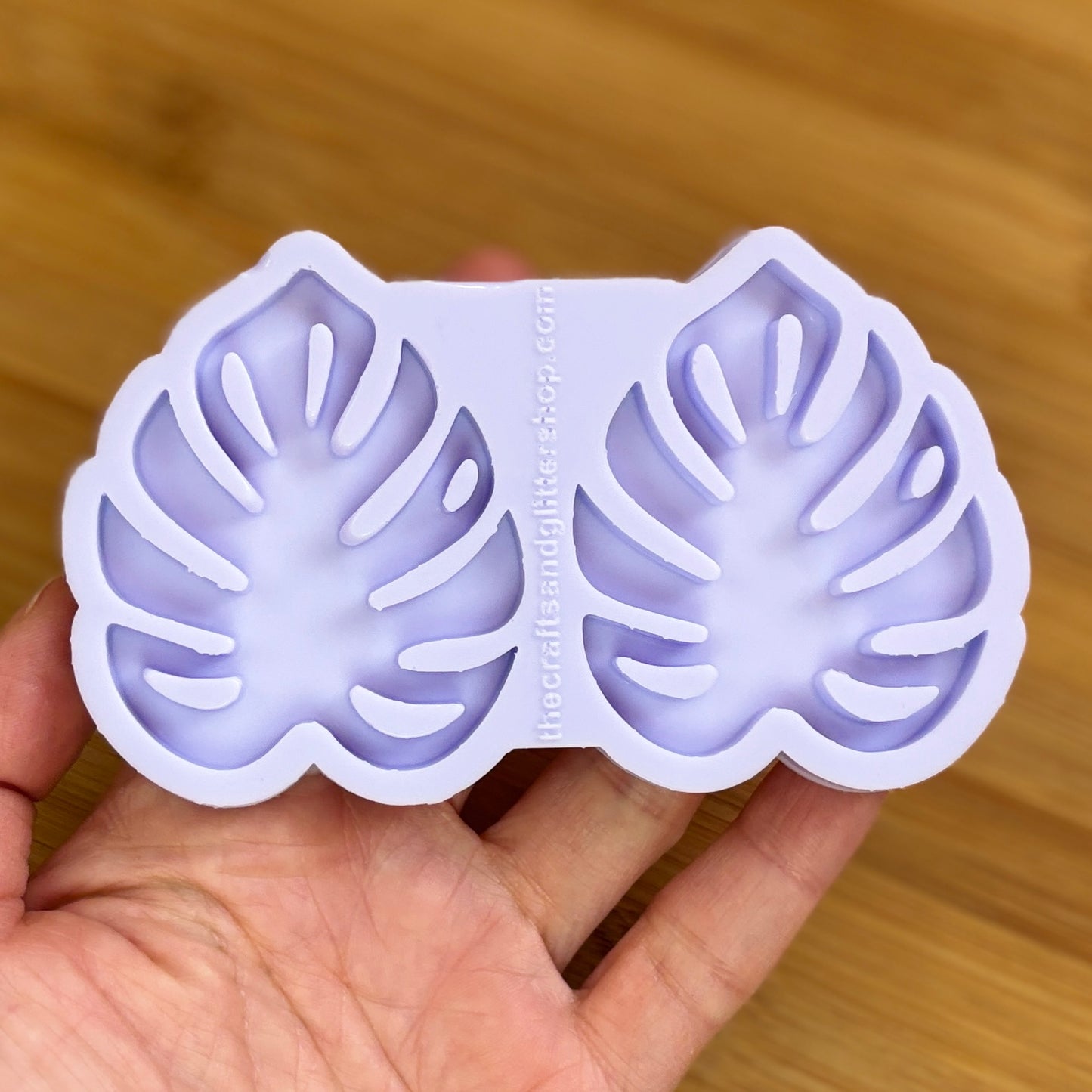 Hand holding a silicone mold with leaf designs on a wooden surface