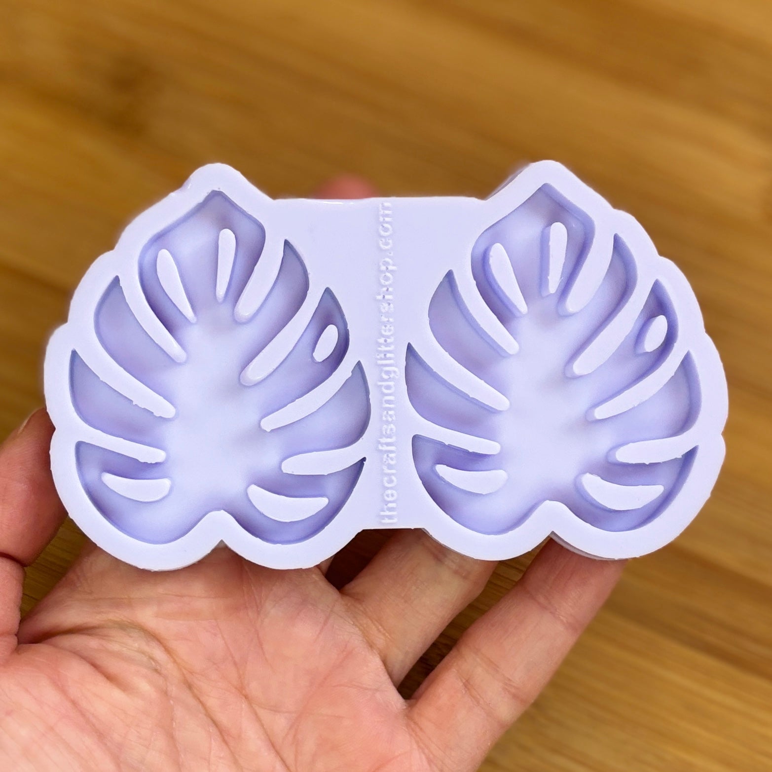 Hand holding a silicone mold with leaf designs on a wooden surface