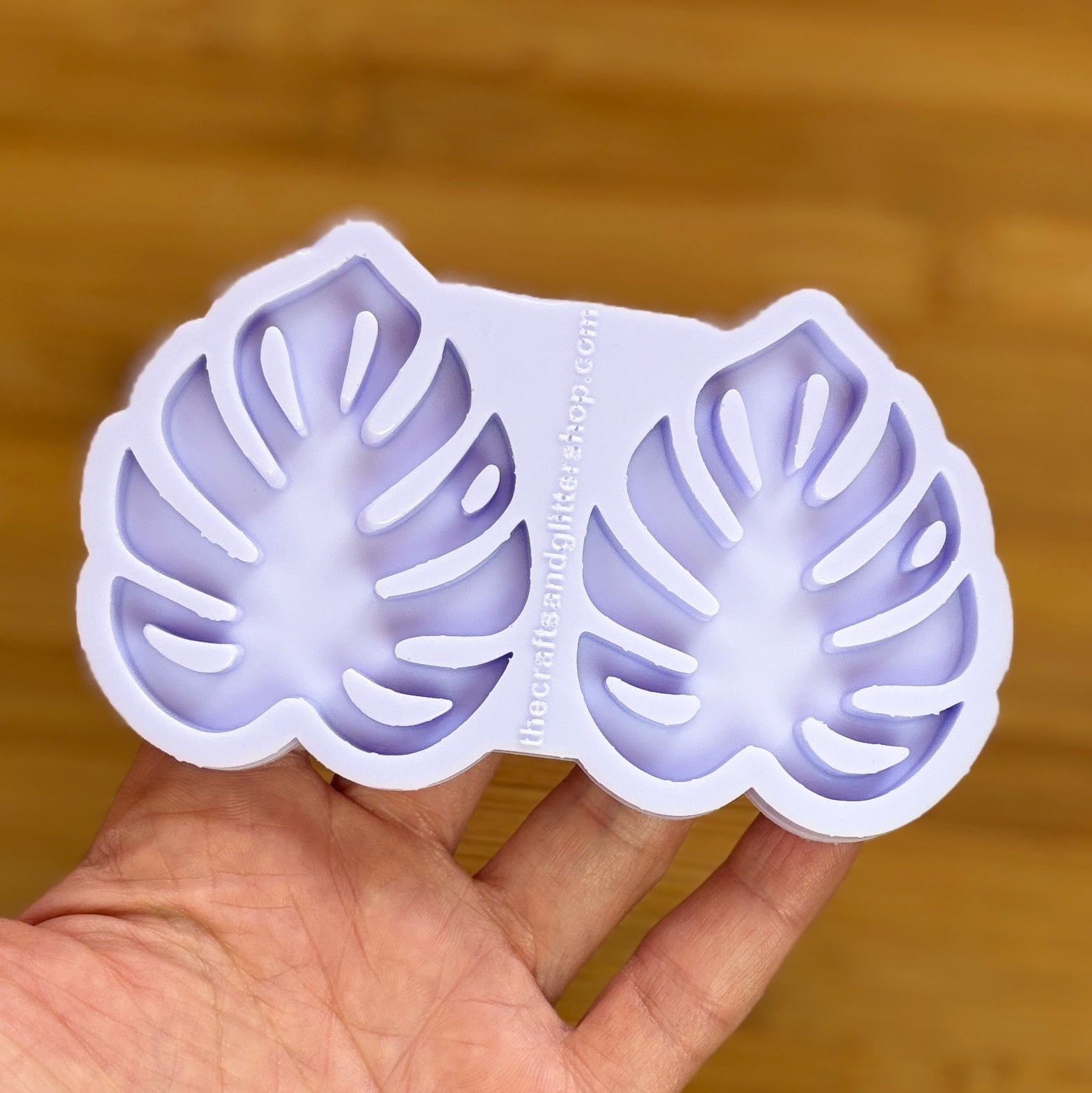 Hand holding a silicone mold with leaf shapes against a wooden background