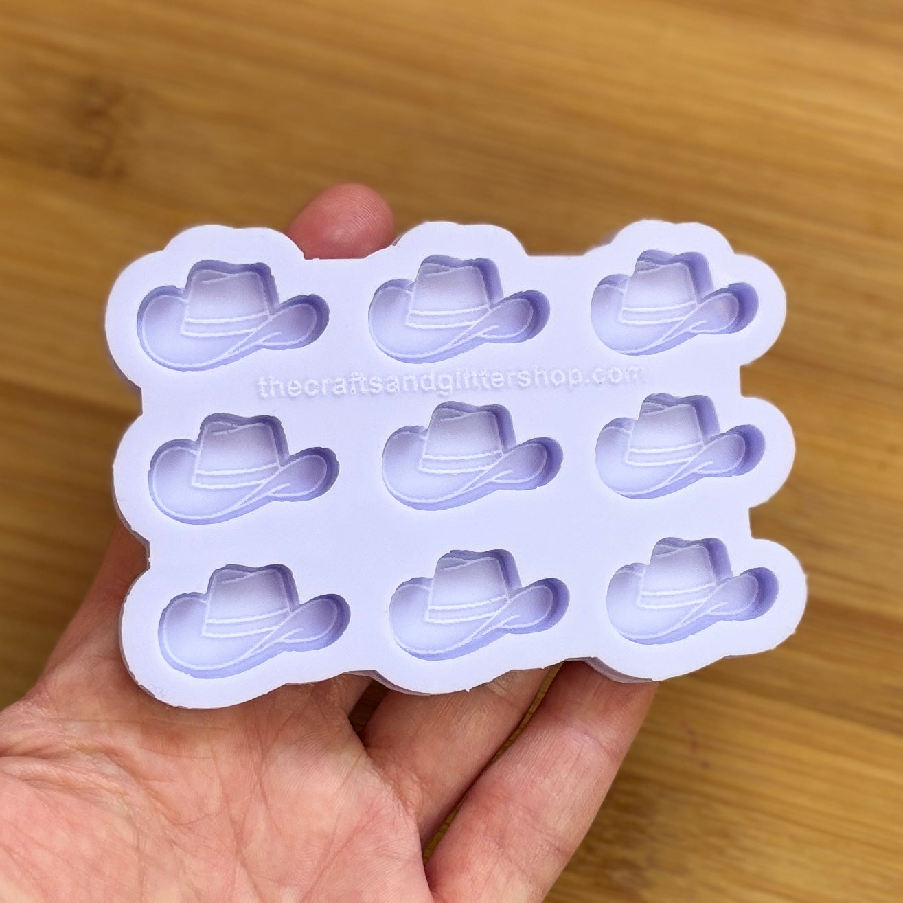Silicone mold with cowboy hat shapes held by a hand on a wooden surface