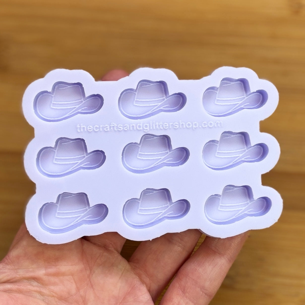 Silicone mold with cowboy hat shapes held by a hand on a wooden surface