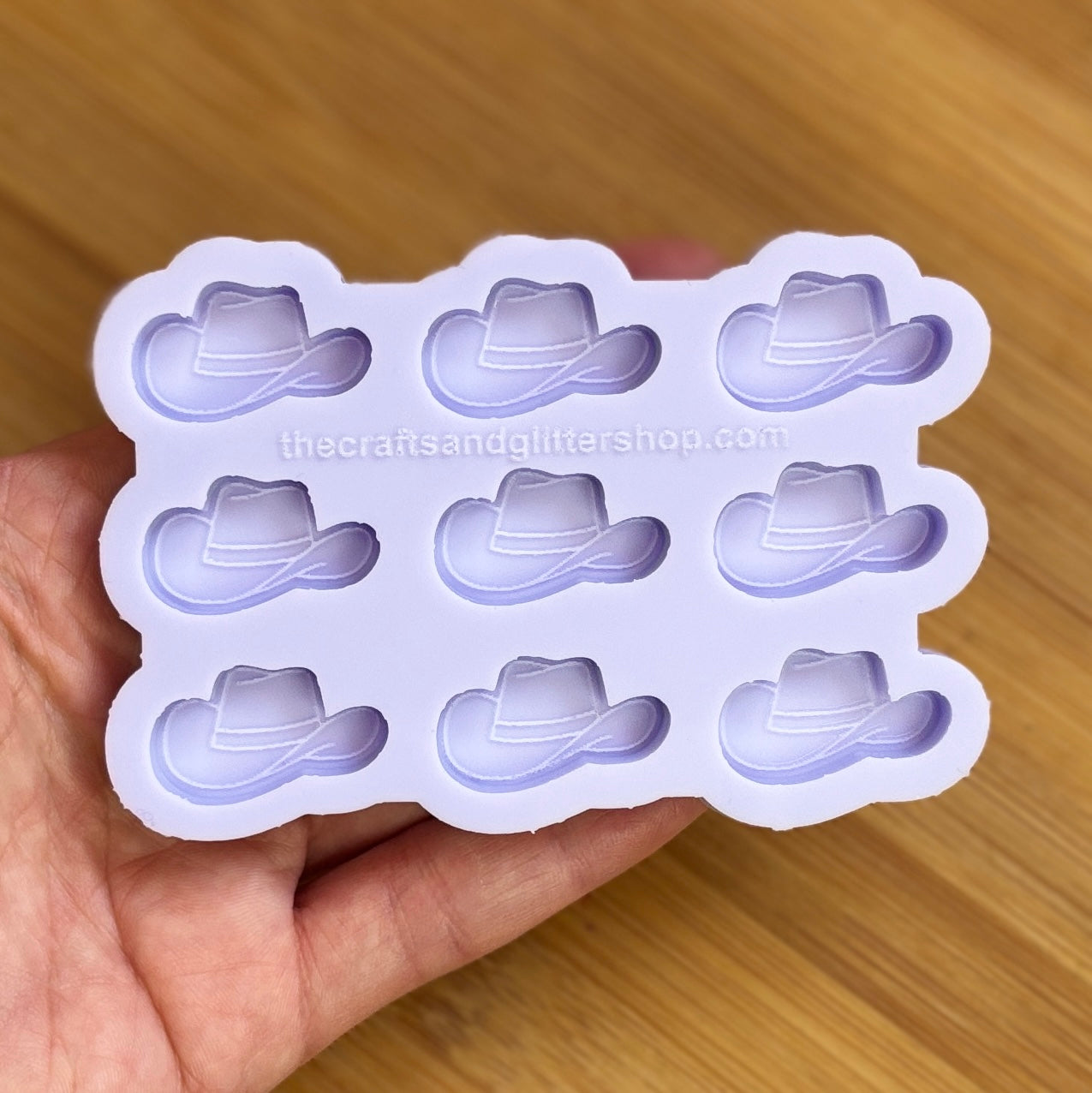 Silicone mold with cowboy hat shapes held by a hand on a wooden surface