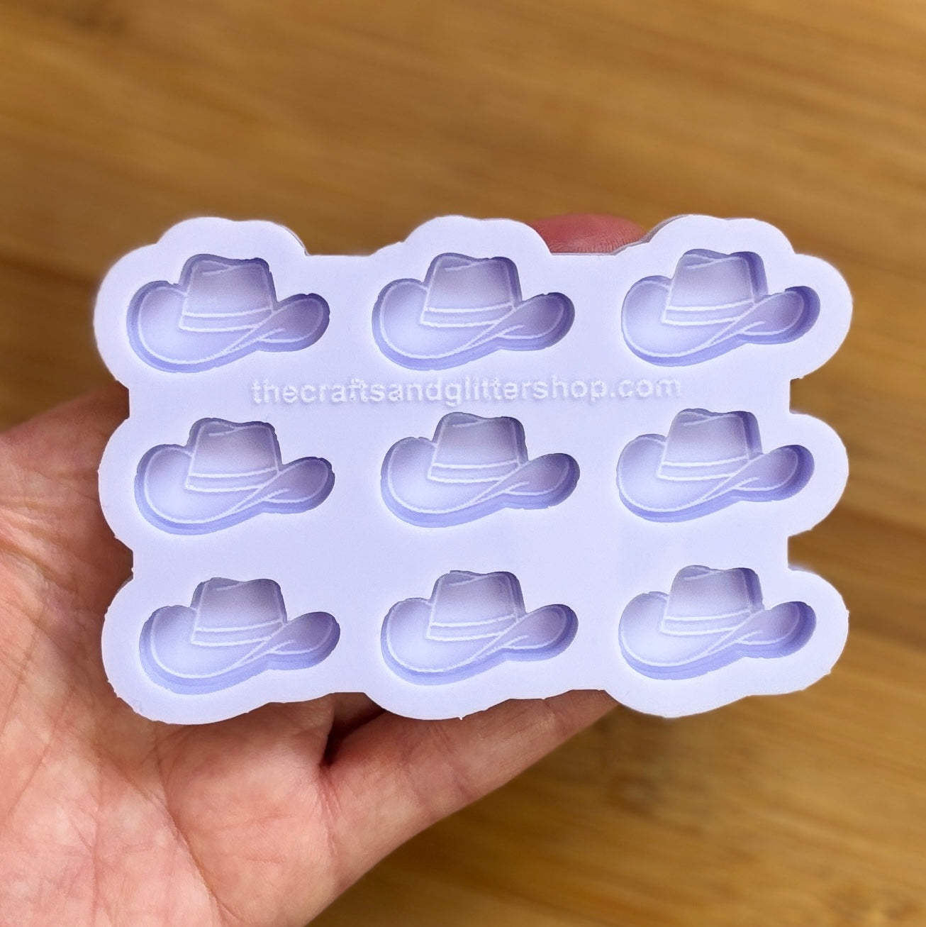 Silicone mold with cowboy hat shapes held by a hand on a wooden surface