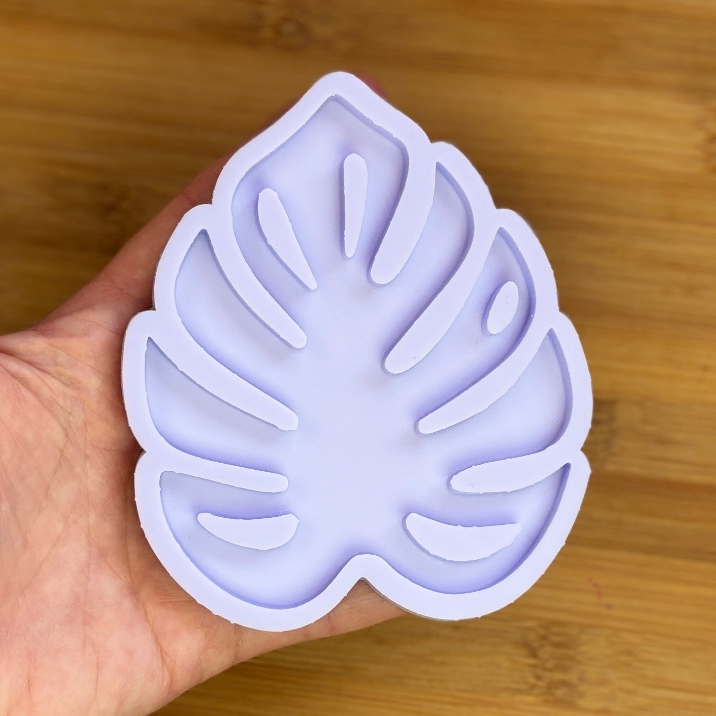 Hand holding a leaf-shaped silicone mold on a wooden surface